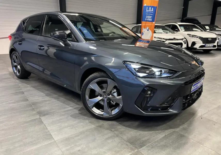 Vue 3/4 avant droite d'une CUPRA Leon gris magnetic avec jantes alliage 18 pouces et phares LED allumés.