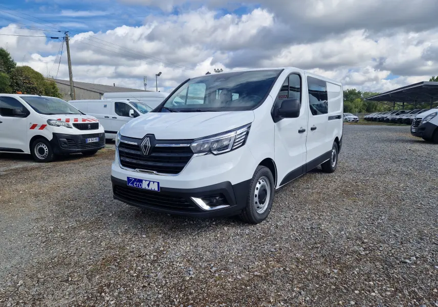 Renault Trafic cabine approfondie blanc en 3/4 avant droit sur parking gravillonné, avec calandre noire et phares modernes.