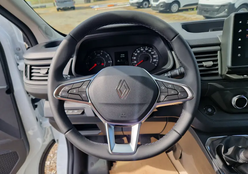 Vue rapprochée du volant noir de la Renault Trafic cabine approfondie blanche, avec tableau de bord et écran tactile visibles.