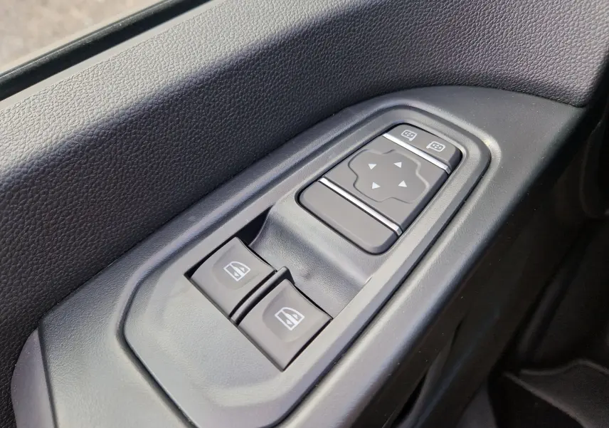 Gros plan sur les commandes de lève-vitres et réglage des rétroviseurs côté conducteur du Renault Trafic blanc.