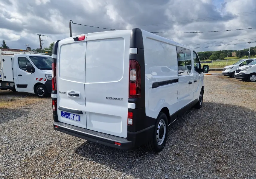 Vue 3/4 arrière droite d’un Renault Trafic Cabine Approfondie blanc, avec portes arrière fermées sur un sol gravillonné.