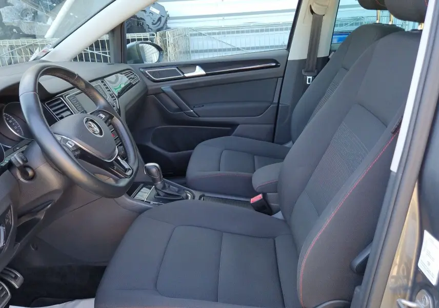 Vue intérieure côté conducteur de la Volkswagen Golf Sportsvan gris Indium, sièges tissu noir avec surpiqûres rouges.