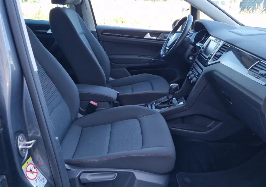 Vue intérieure côté conducteur d'une Volkswagen Golf Sportsvan gris Indium, sièges tissu noirs et tableau de bord moderne.