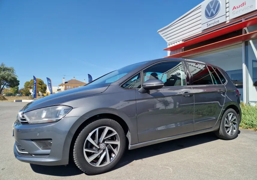 Volkswagen Golf Sportsvan gris Indium métal vue 3/4 avant droit, stationnée devant un service Volkswagen Audi.