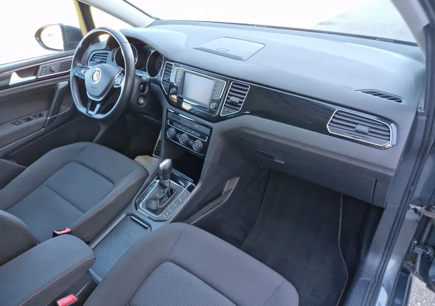 Vue intérieure côté conducteur de la Volkswagen Golf Sportsvan 1.6 TDI 2017, avec tableau de bord noir et console centrale moderne.