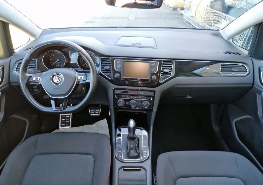 Vue intérieure frontale du tableau de bord gris et noir de la Volkswagen Golf Sportsvan 2017 avec volant multifonction et boîte automatique.