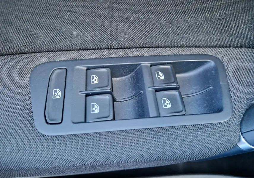 Gros plan sur les commandes de lève-vitres côté conducteur, sur tissu gris foncé à l'intérieur d'une Volkswagen Golf Sportsvan.
