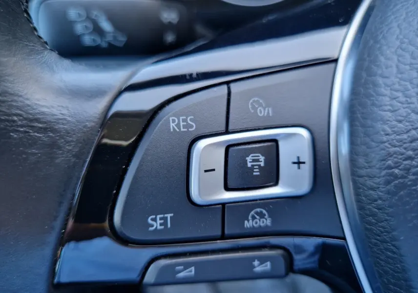 Gros plan sur les commandes de régulateur de vitesse au volant cuir noir d'une Volkswagen Golf Sportsvan gris Indium Metal.