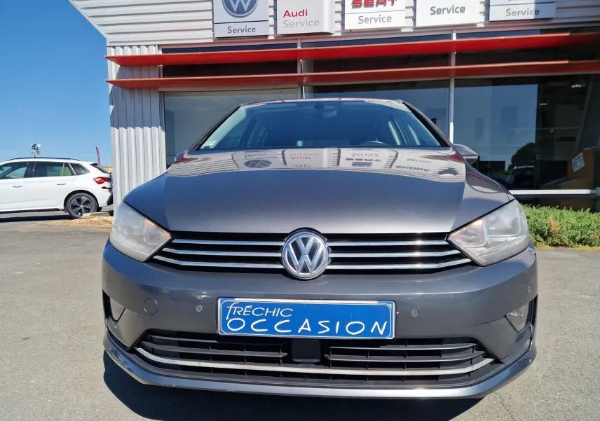 Vue frontale d'une Volkswagen Golf Sportsvan gris Indium Metal, avec calandre horizontale et plaque d'occasion bleue visible.