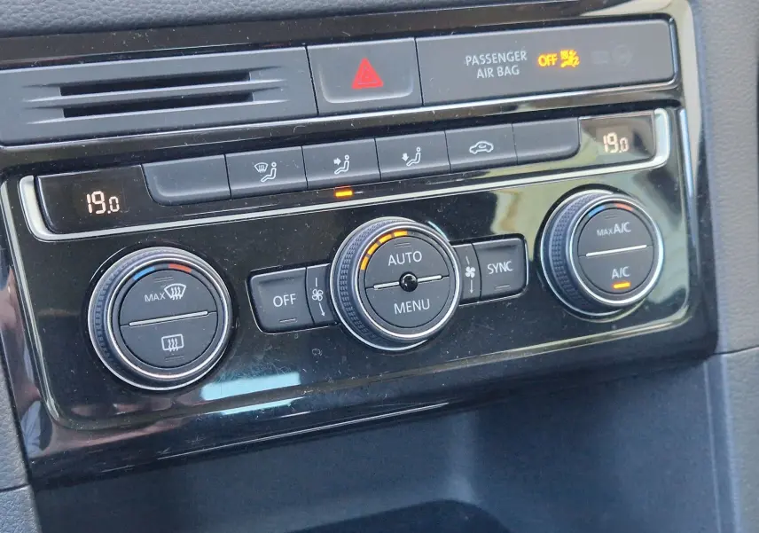 Gros plan sur la console de climatisation noire brillante du Volkswagen Golf Sportsvan gris Indium, avec affichage digital et boutons ronds.