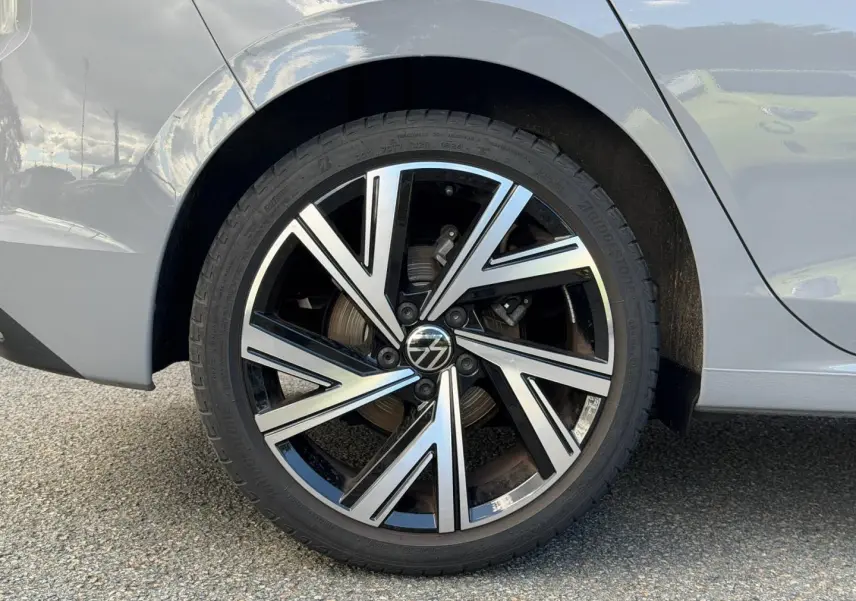 Gros plan sur la roue arrière droite d'une Volkswagen Golf gris lunaire avec jante alu bicolore moderne.