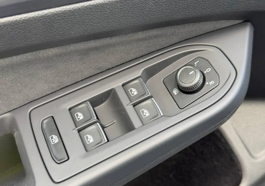 Gros plan sur les commandes de lève-vitres et réglage des rétroviseurs côté conducteur de la Volkswagen Golf gris lunaire 2024.