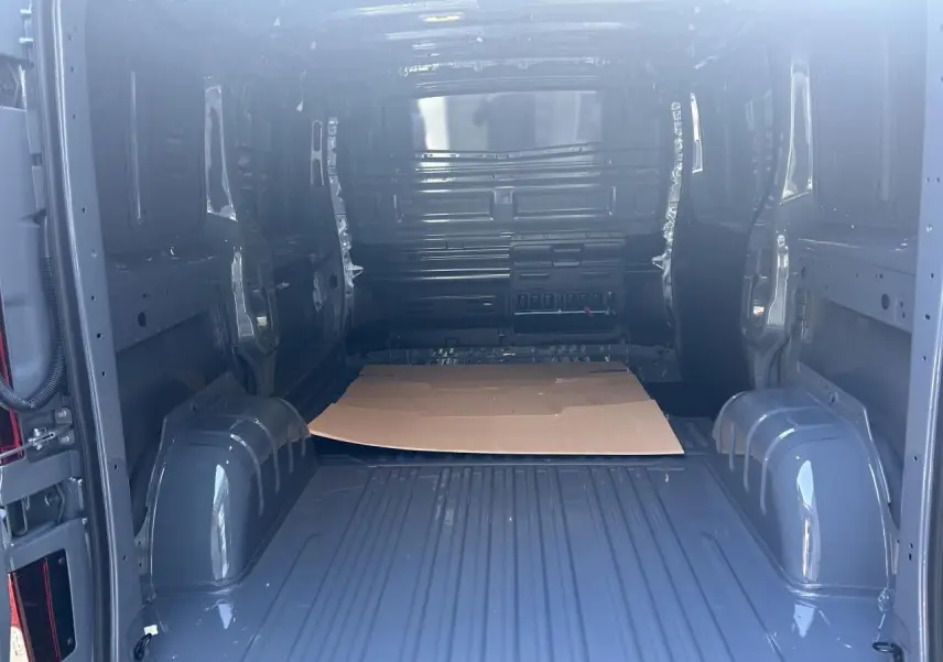 Intérieur du fourgon Renault Trafic L1H1 Gris Urbain vu de l'arrière, montrant l'espace de chargement vide et les passages de roues.
