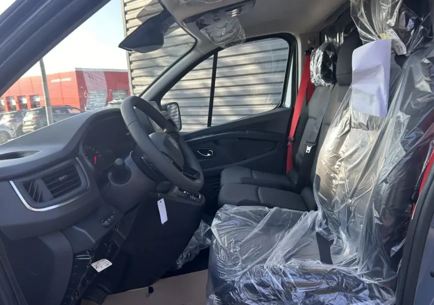 Intérieur du Renault Trafic Fourgon 2025 vu côté conducteur, sièges avant protégés par film plastique et ceinture rouge visible.
