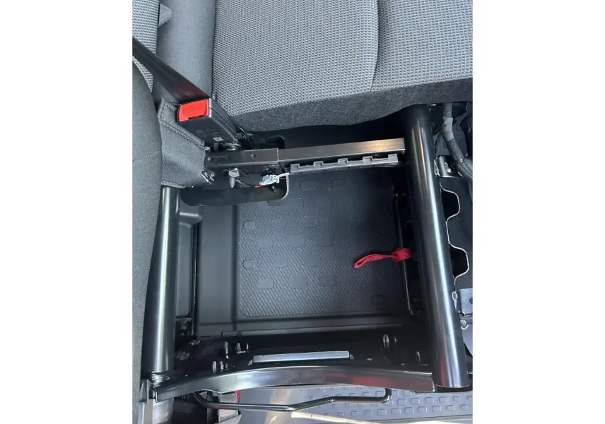 Gros plan sous la banquette rabattable du Renault Trafic Fourgon gris urbain, montrant la structure métallique et la sangle rouge.