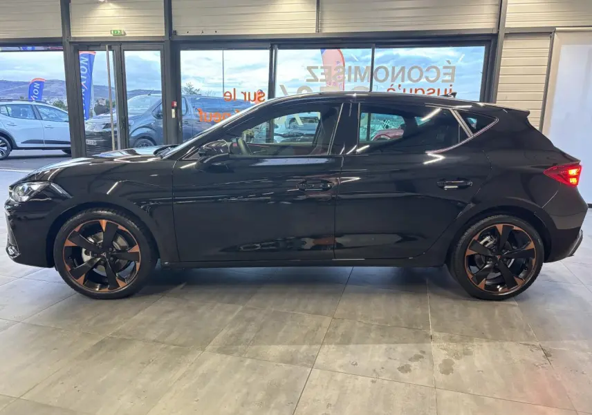 Vue de profil côté gauche d'une CUPRA Leon noir midnight avec jantes alliage 18'' cuivrées dans un showroom.