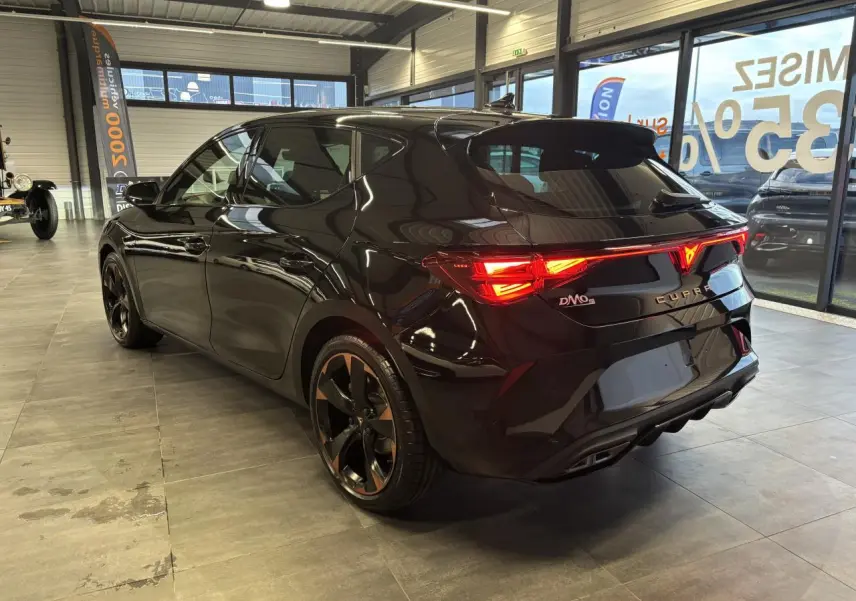 Vue 3/4 arrière droite d'une CUPRA Leon noir midnight avec feux arrière Tri-LED et jantes alliage 18'' cuivrées.
