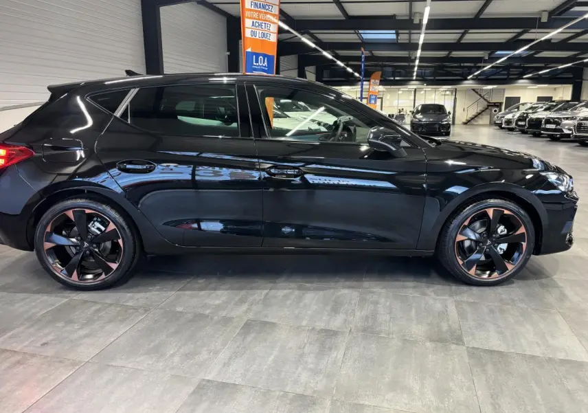 Profil droit d'une CUPRA Leon noir midnight avec jantes alliage 18'' cuivrées en showroom lumineux.