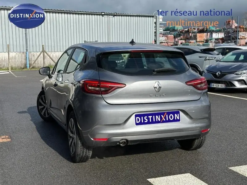 Vue 3/4 arrière d'une Renault Clio gris métallisé 2023, avec feux arrière LED et logo distinctif sur un parking.