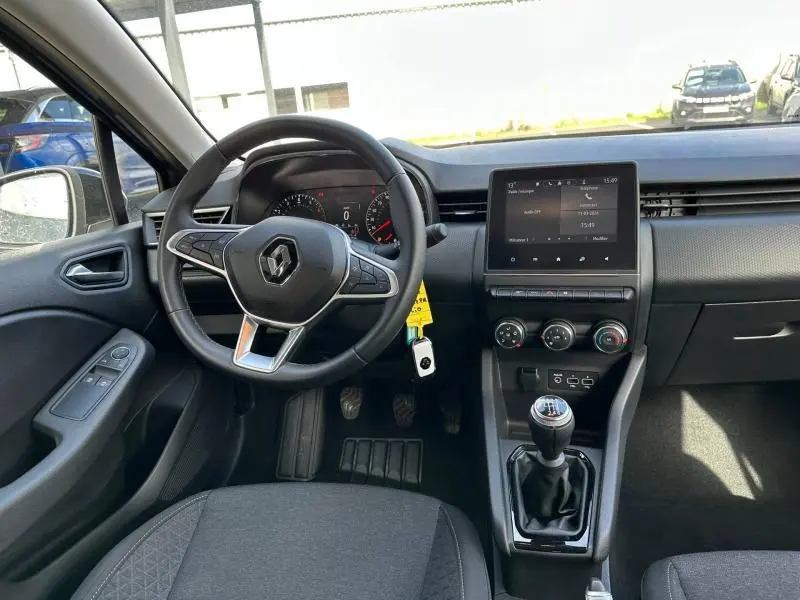 Vue intérieure avant de la Renault Clio gris 2023, volant multifonction, écran tactile central et boîte manuelle visible.