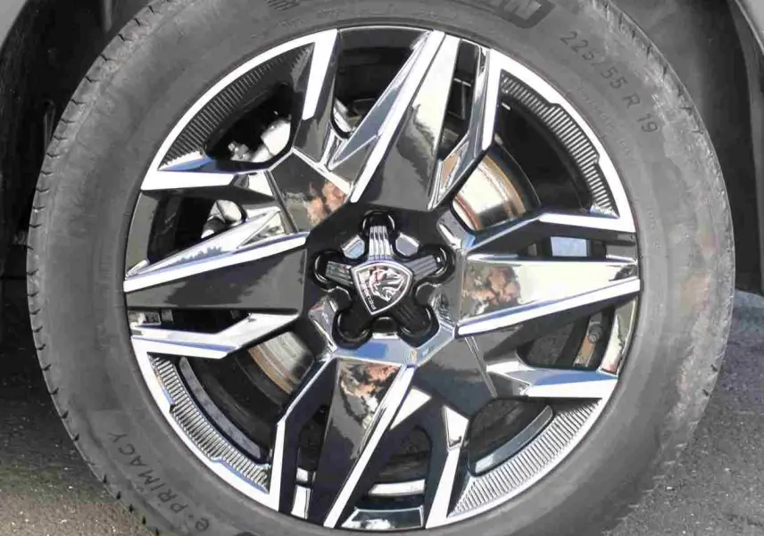 Gros plan sur la jante alliage noire et argentée avec logo Peugeot, montée sur pneu Michelin d’un Peugeot 5008 gris titane.