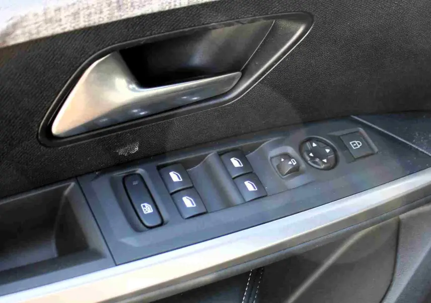 Gros plan sur la commande des vitres et la poignée intérieure côté gauche d’un Peugeot 5008 gris titane hybride.