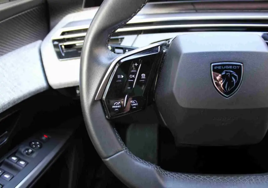 Gros plan sur le volant cuir noir du Peugeot 5008 2025 avec commandes intégrées et logo lion chromé central.