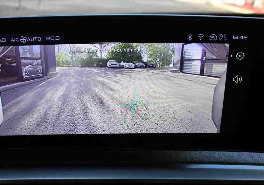 Vue de l'écran intérieur du Peugeot 5008 Hybrid gris titane montrant la caméra de recul avec parking extérieur visible.