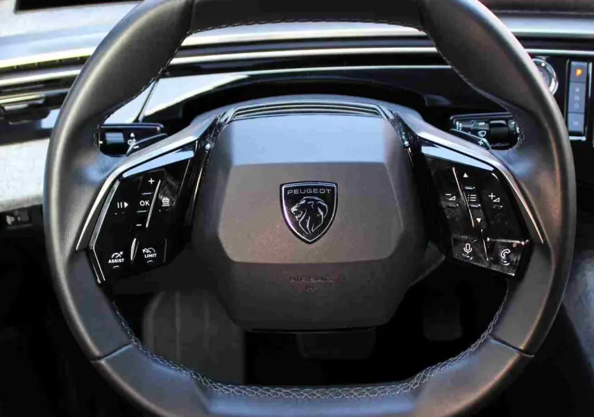 Vue rapprochée du volant cuir noir du Peugeot 5008 2025, avec commandes intégrées et logo lion central.