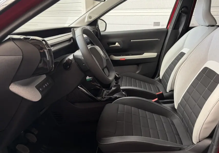 Vue intérieure côté conducteur de la Citroën C3 2025, sièges bicolores noirs et gris avec volant cuir multifonctions.