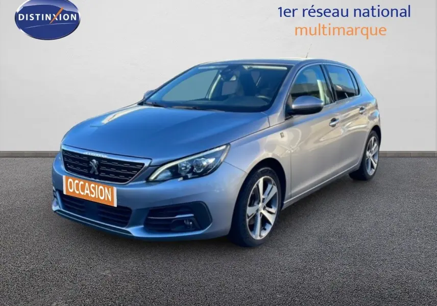 Peugeot 308 gris Artense métal vue 3/4 avant droit sur fond neutre avec plaque occasion orange.