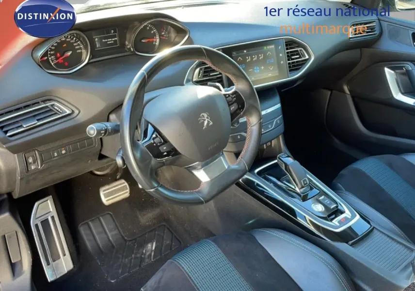 Vue intérieure côté conducteur de la Peugeot 308 gris Artense, avec volant cuir et écran tactile central visible.