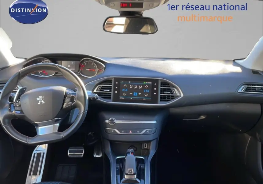 Vue intérieure avant du tableau de bord et volant noir de la Peugeot 308 gris Artense, avec écran tactile central allumé.