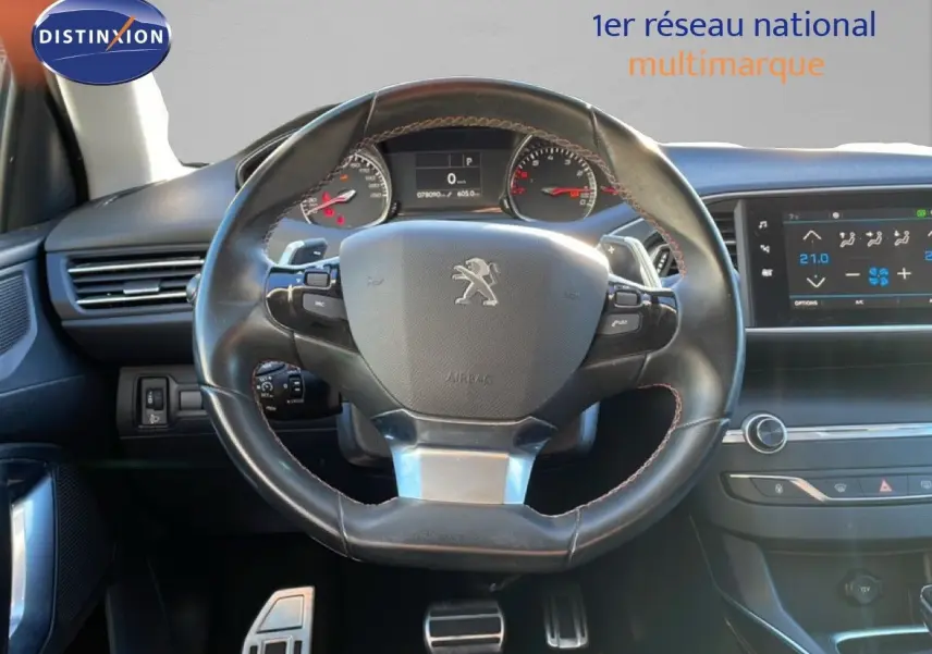 Vue intérieure centrée sur le volant cuir noir de la Peugeot 308 gris Artense, avec tableau de bord et écran tactile visibles.