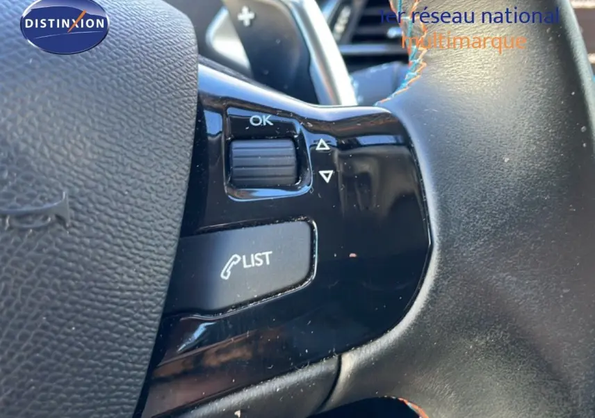 Gros plan sur les commandes au volant noir de la Peugeot 308 gris Artense, avec bouton "LIST" et molette "OK".
