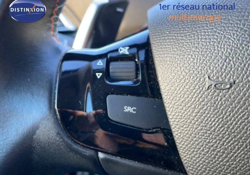 Gros plan sur les commandes noires du volant de la Peugeot 308 gris Artense, mettant en valeur les boutons SRC et volume.