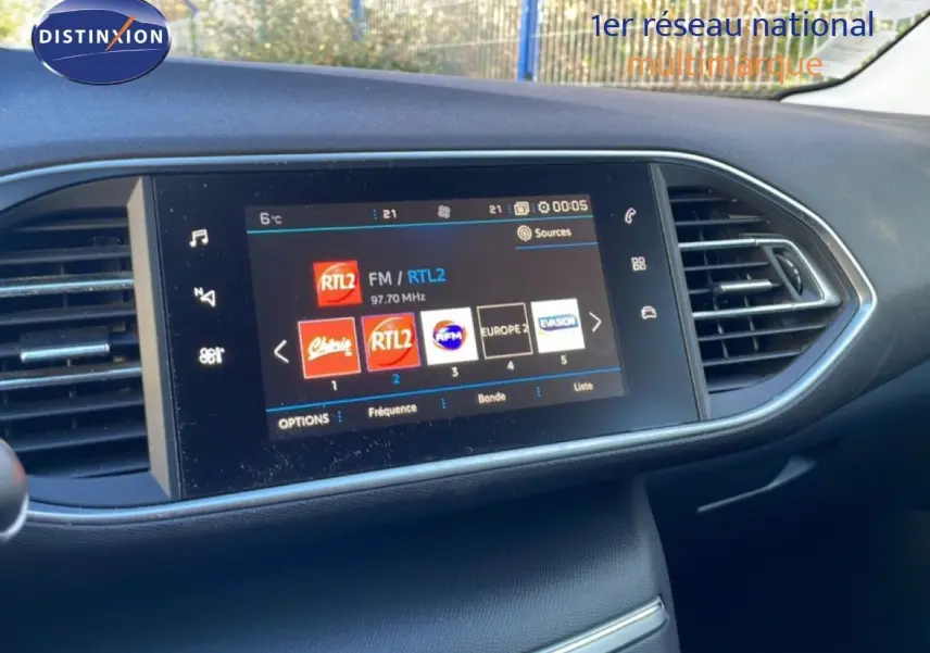 Écran tactile central de la Peugeot 308 gris Artense, affichant les stations radio avec commandes autour et aérateurs latéraux.
