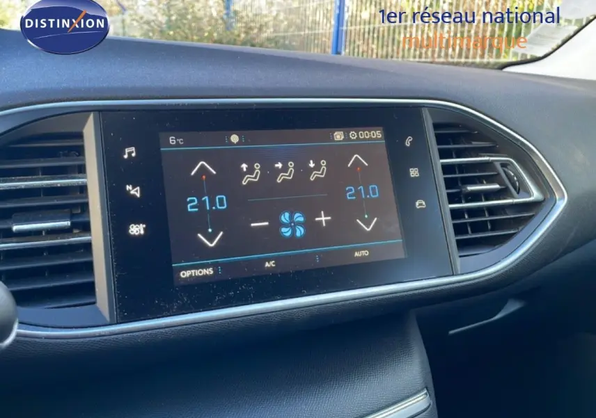 Écran tactile central du tableau de bord de la Peugeot 308 affichant la climatisation à 21°C, entouré de grilles d'aération noires.