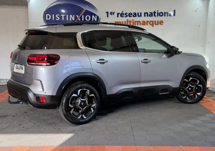 Vue latérale droite d'un Citroën C5 Aircross gris clair 2023, avec jantes noires et toit noir contrasté en intérieur showroom.