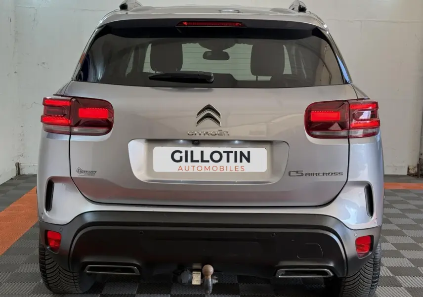 Vue arrière d'un Citroën C5 Aircross gris clair 2023 avec feux LED et attelage visible en intérieur showroom.