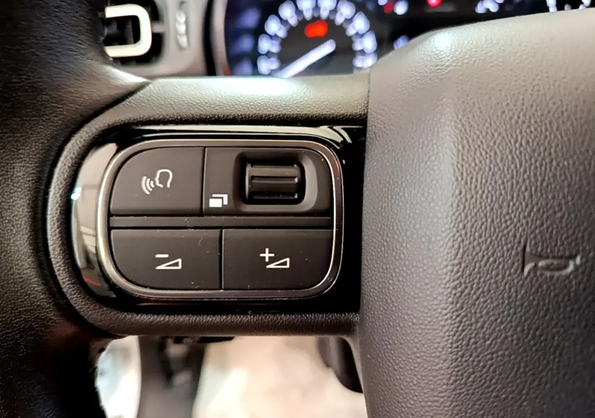 Gros plan sur les commandes vocales et volume au volant cuir noir d'une Citroën C3 blanche, tableau de bord flou en arrière-plan.