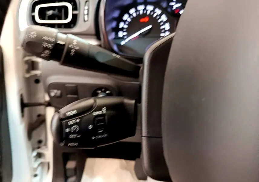 Gros plan sur le volant cuir et les commandes au volant d'une Citroën C3 blanche, tableau de bord lumineux en arrière-plan.