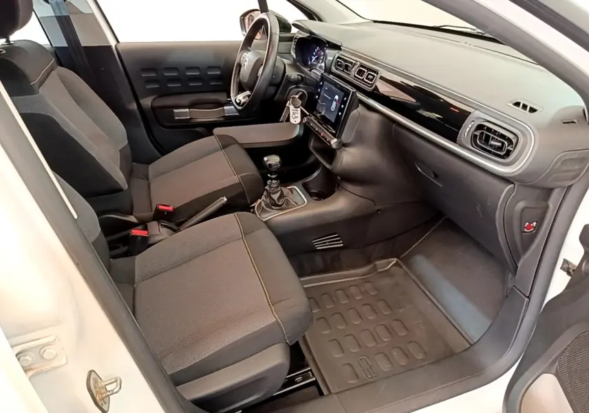 Intérieur côté conducteur de la Citroën C3 blanche, vue 3/4 avant, avec tableau de bord noir et écran tactile central.
