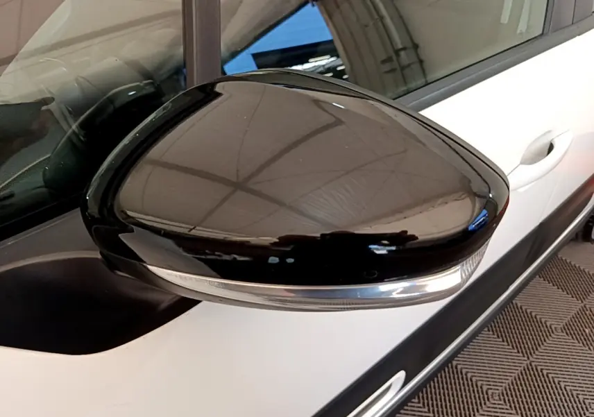 Gros plan sur le rétroviseur droit noir brillant d'une Citroën C3 blanche, avec poignée de porte visible en arrière-plan.