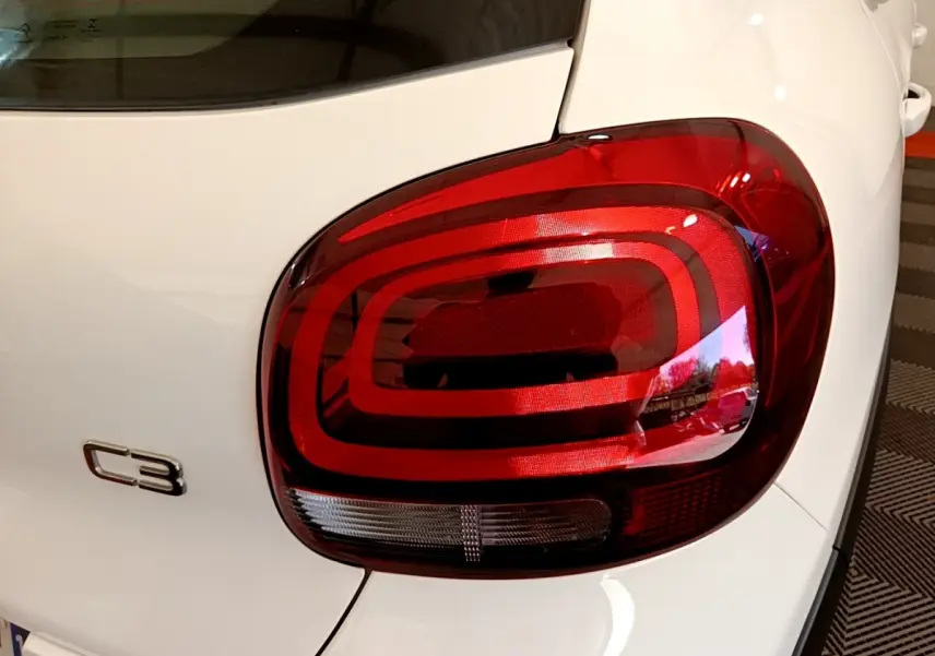 Gros plan sur le feu arrière droit rouge d'une Citroën C3 blanche, mettant en valeur le logo C3 sur la carrosserie.