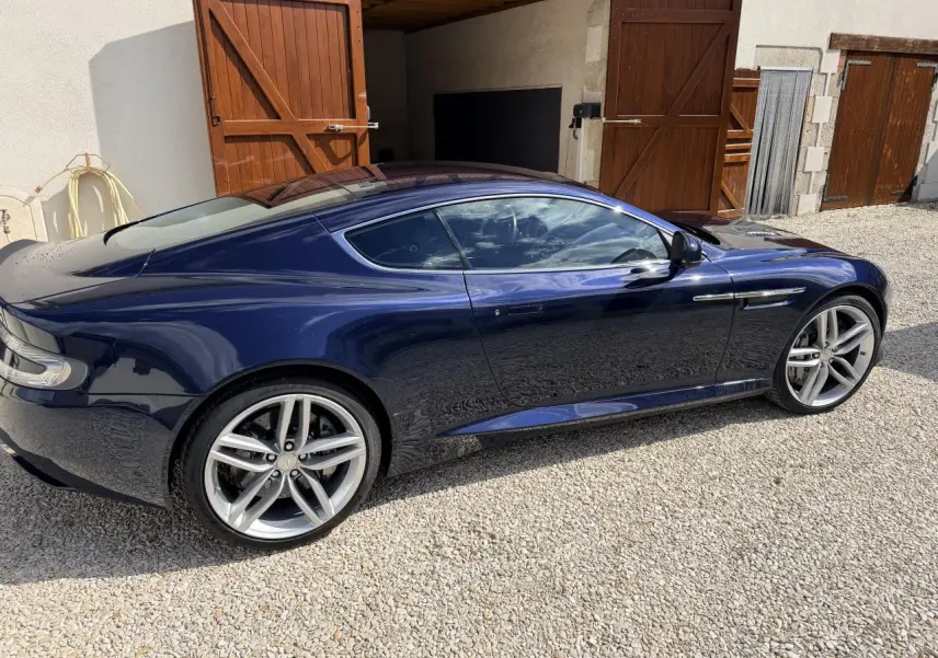 Vue latérale droite d'une Aston Martin DB9 bleu foncé 2016, soulignant ses jantes alliage et sa silhouette élégante.