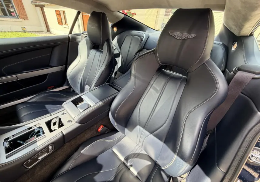Intérieur de l'Aston Martin DB9 2016, vue côté droit sur sièges sport en cuir noir avec logo Aston Martin brodé.