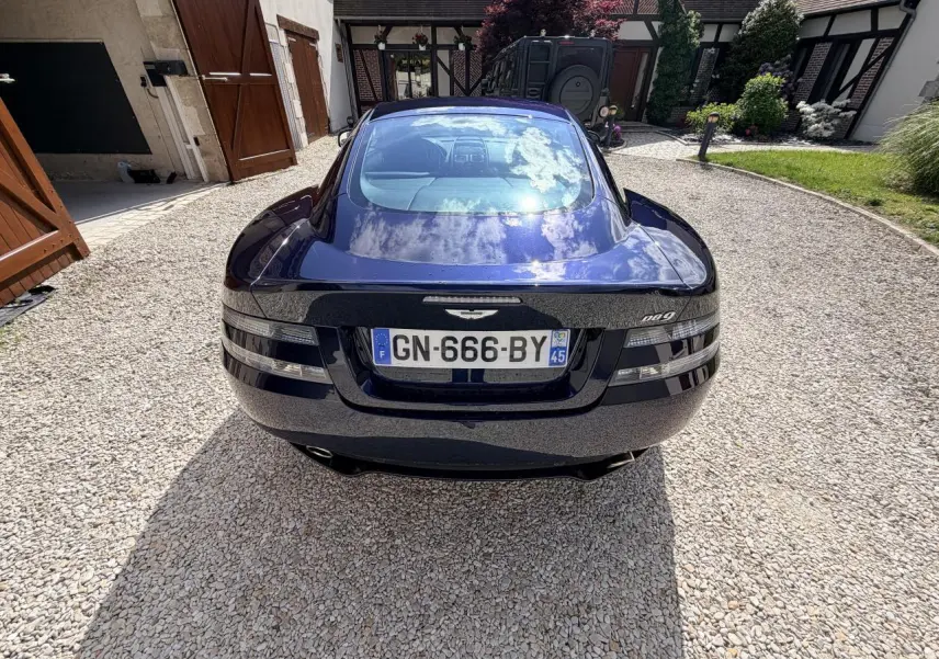 Vue arrière d'une Aston Martin DB9 bleu foncé 2016, avec ses feux distinctifs et une plaque d'immatriculation française.