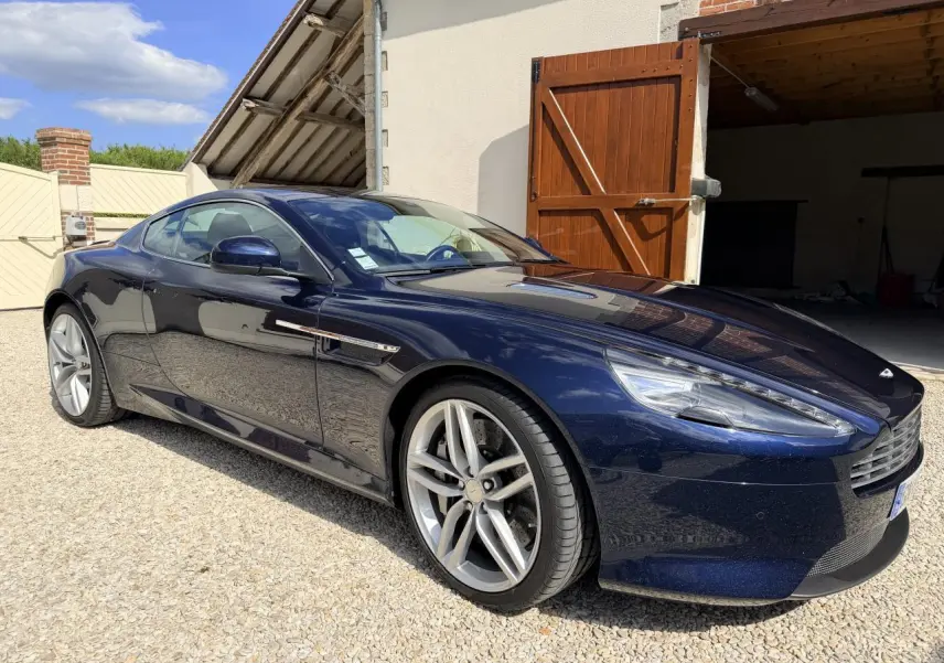 Aston Martin DB9 bleu foncé vue 3/4 avant droit, mettant en valeur ses jantes argentées et sa calandre distinctive.