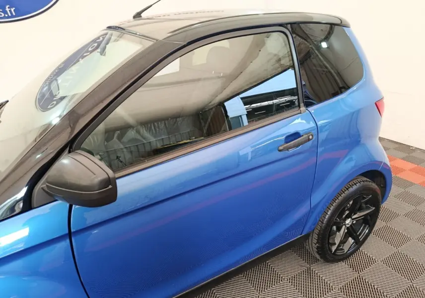Vue côté gauche en 3/4 arrière d'une Aixam Ambition 0.5 City Sport bleu avec rétroviseur conducteur noir.